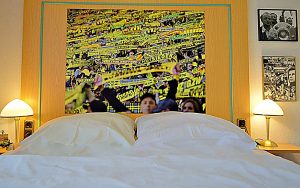 Innenansicht: großes Hotelzimmer, breites Bett, Riesenbild von BVB Fankurve über Bett